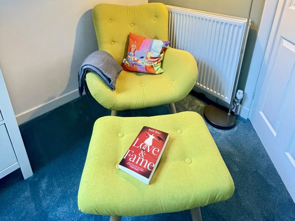 A sitting room with a green armchair and ottoman with a book at Portknockie Cottage Buckie