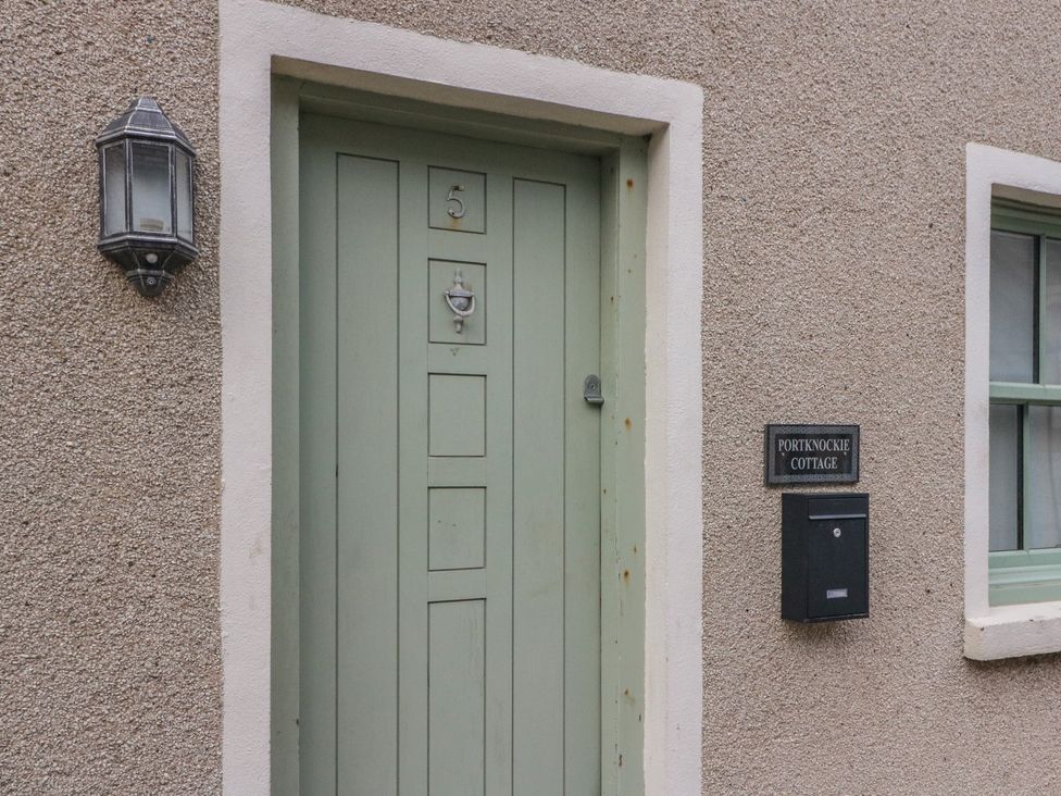 An entrance door with a sign and light fixture at Portknockie Cottage in Portknockie