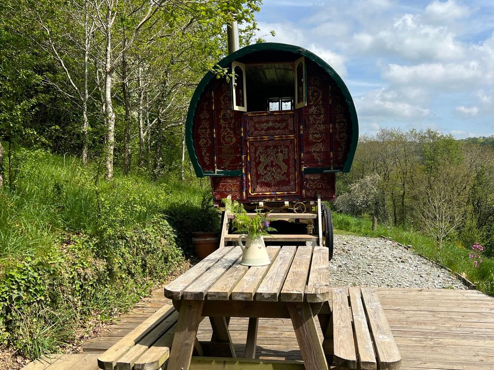 A caravan and wooden table with flowers at Goldfinch in Panson Mill near Ashwater