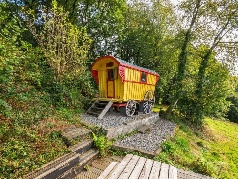 A gypsy caravan on a gravel base surrounded by trees and grass at Prudence Panson Mill near Ashwater