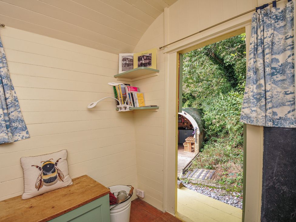 A small room with a bench, shelves, and a door leading outside at Prudence in Panson Mill near Ashwater