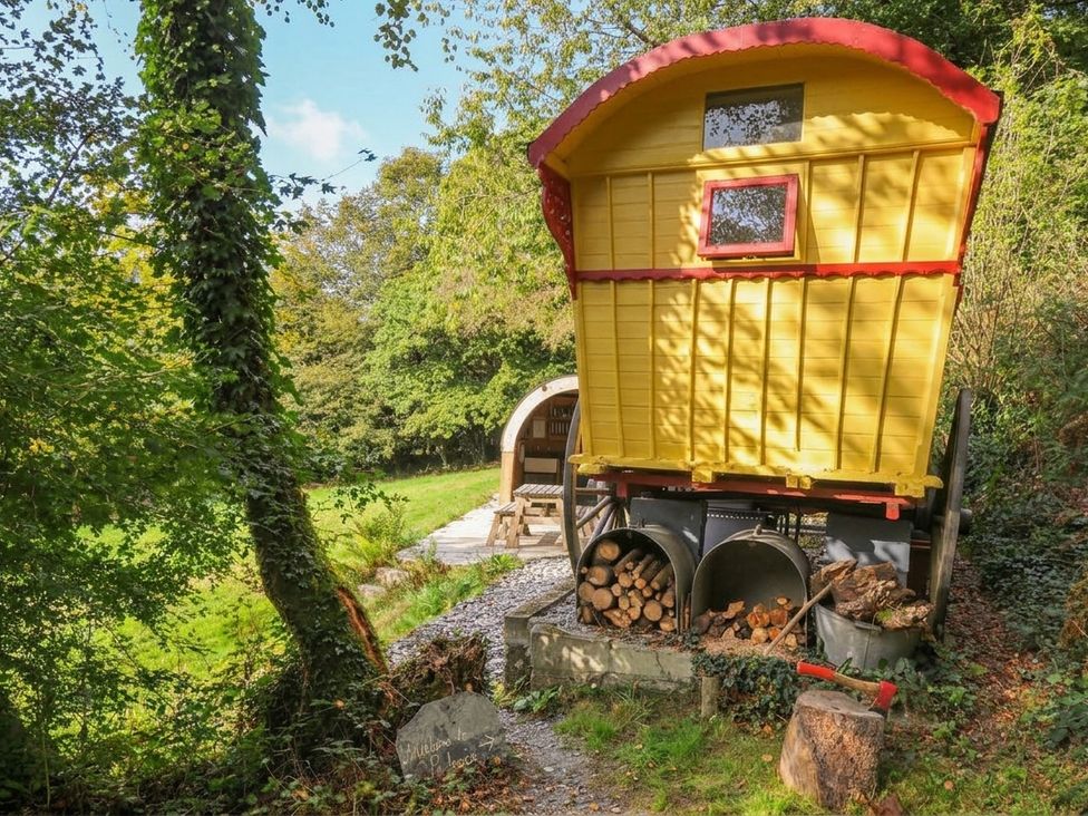 A yellow caravan with wood storage and outdoor seating at Prudence, Panson Mill near Ashwater