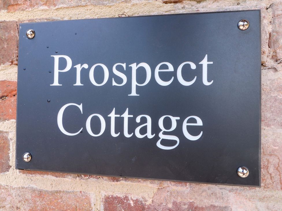 A sign displaying the name Prospect Cottage on a brick wall