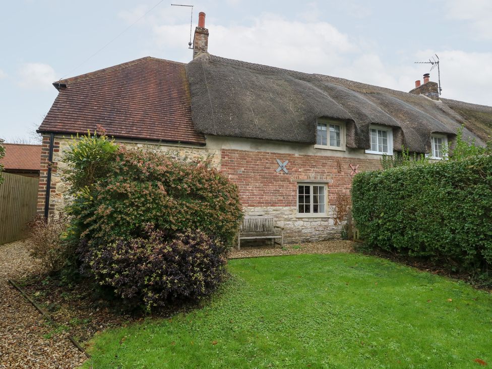 A garden with a thatched roof cottage and hedges at Bubbs Cottage