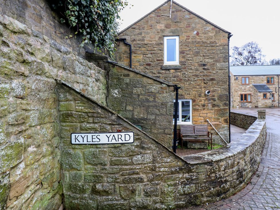 A sign indicating Kyles Yard next to a stone wall and building at 1 Kyles Yard in Barnard Castle