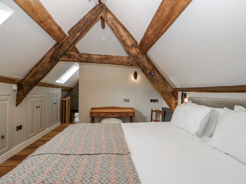 A bedroom with wooden beams, a bed, desk, and wardrobe at 1 bed property Usk