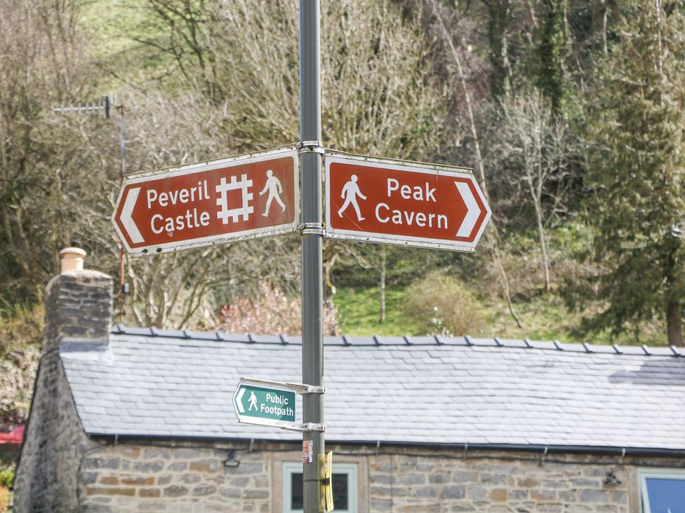 A signpost indicating directions to Peveril Castle and Peak Cavern near a stone building in Hope Valley