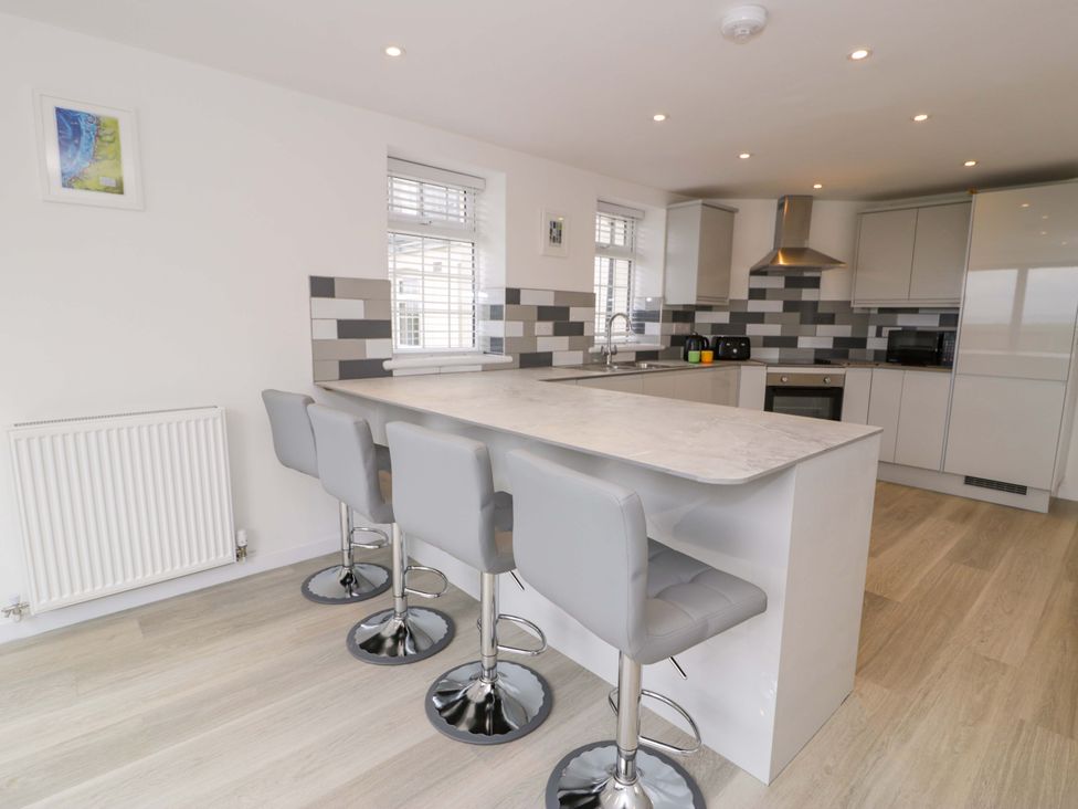A kitchen with bar stools and kitchen appliances at Rosemary Cottage 1 in Tywyn