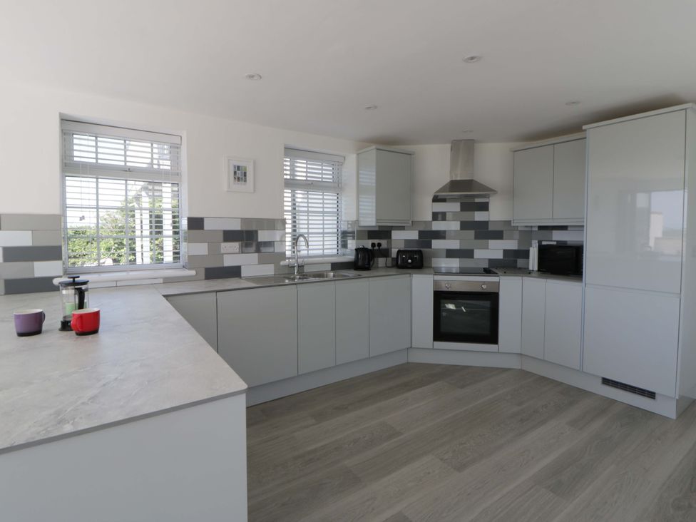 A kitchen with gray cabinets and appliances at Rosemary Cottage 1 Tywyn