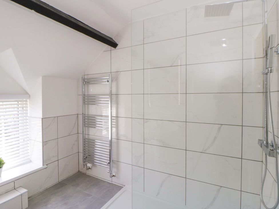 A bathroom with shower, bath, and towel radiator at Rosemary Cottage 1 in Tywyn