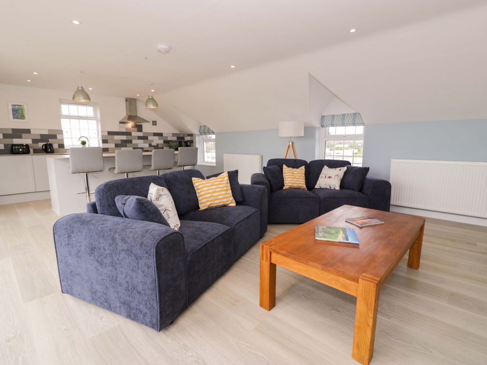 A living room with a sofa, coffee table, and kitchen area at Rosemary Cottage 2 in Tywyn