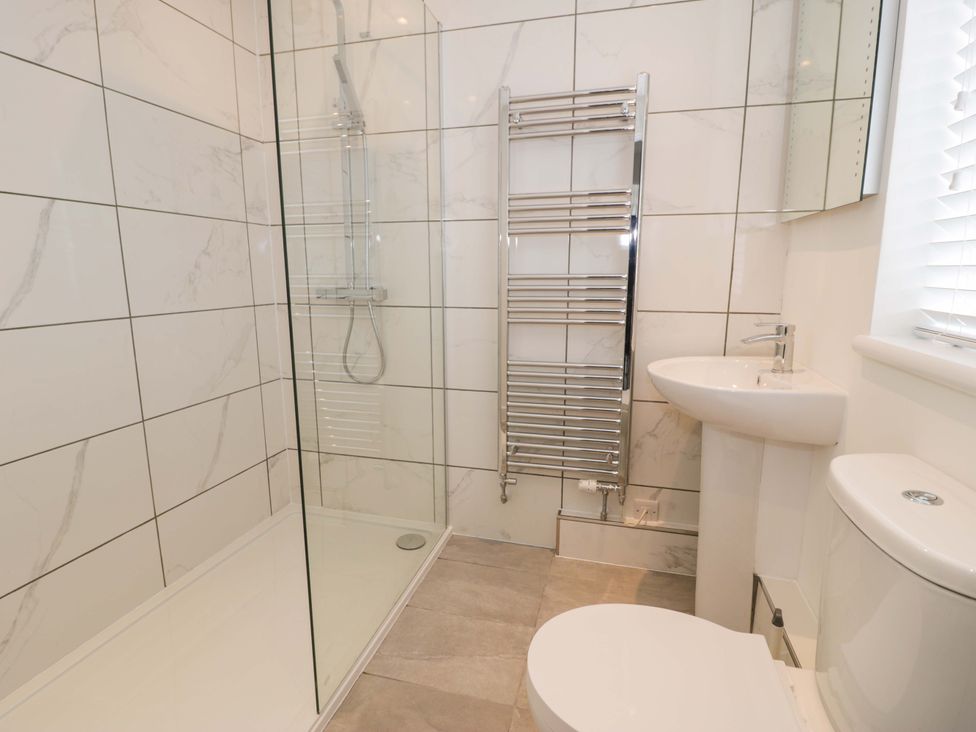 A bathroom with a shower, toilet, sink, and towel radiator at Rosemary Cottage 2, Tywyn