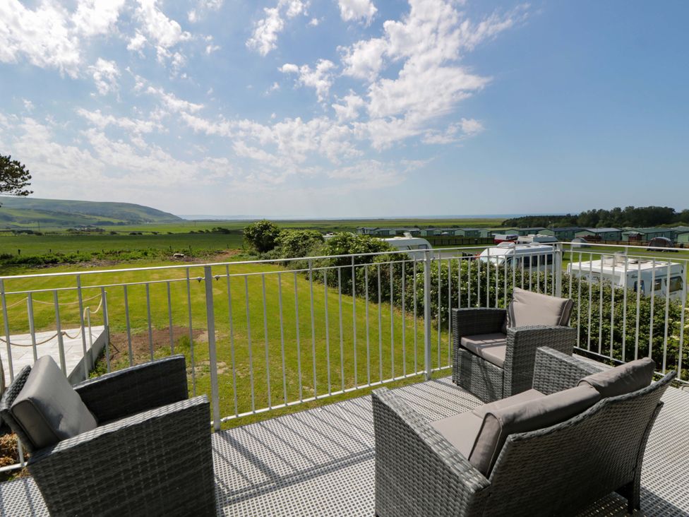 A balcony with chairs overlooking a grassy area and hills at Rosemary Cottage 2 Tywyn