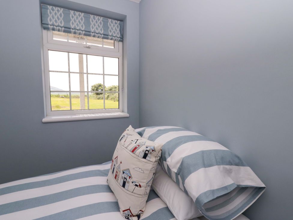 A bedroom with a window and striped bed linen at Rosemary Cottage 2 Tywyn
