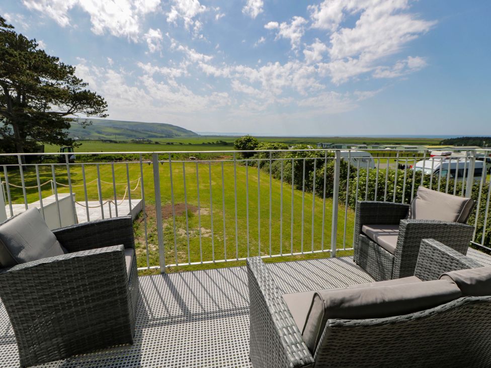 A balcony with chairs overlooking a grassy area and hills at Rosemary Cottage 2 Tywyn