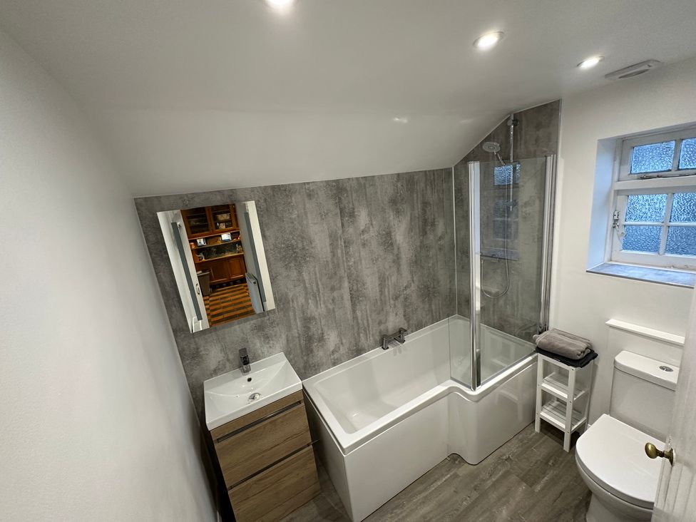 A bathroom with a bathtub, mirror, sink, and toilet at Hop Cottage in Petersfield