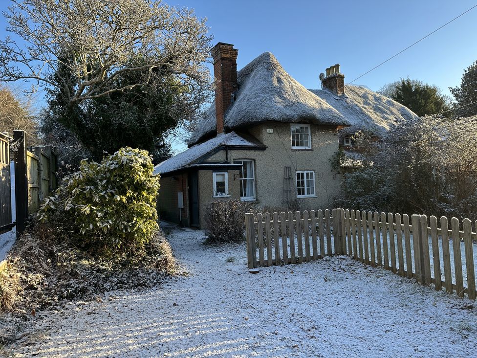 A cottage with a thatched roof and a fenced garden at Hop Cottage in Buriton