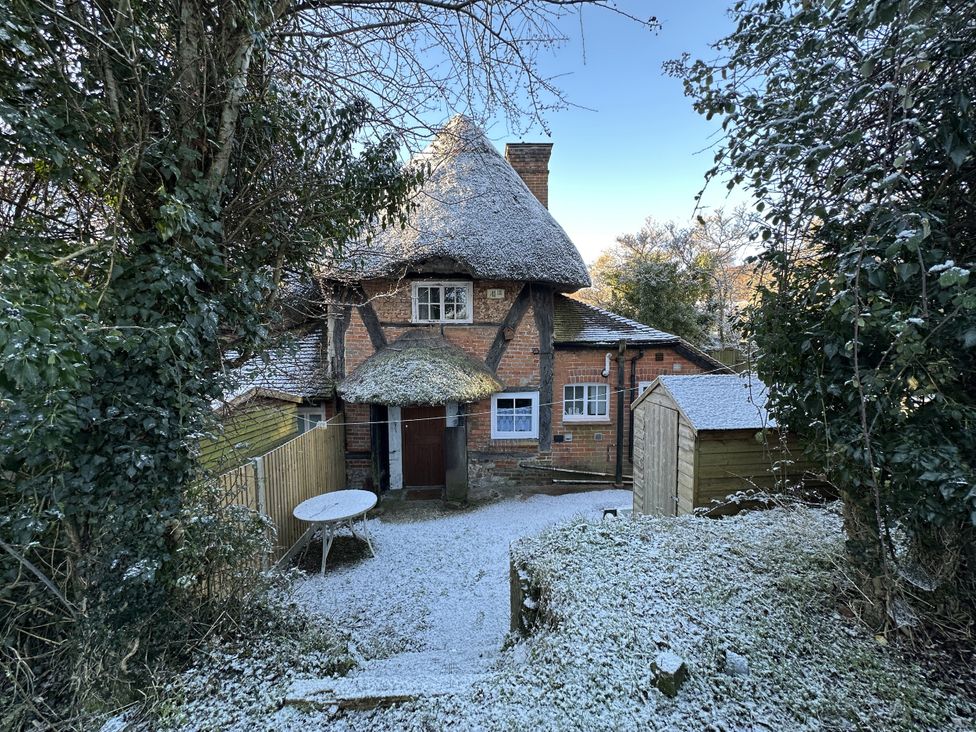 An outdoor view of a house with a thatched roof and a shed at Hop Cottage Buriton