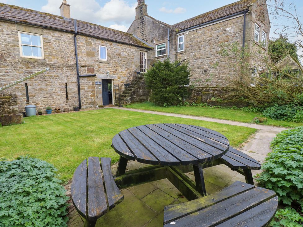 A garden with a stone building and wooden table at The Hay Barn in 