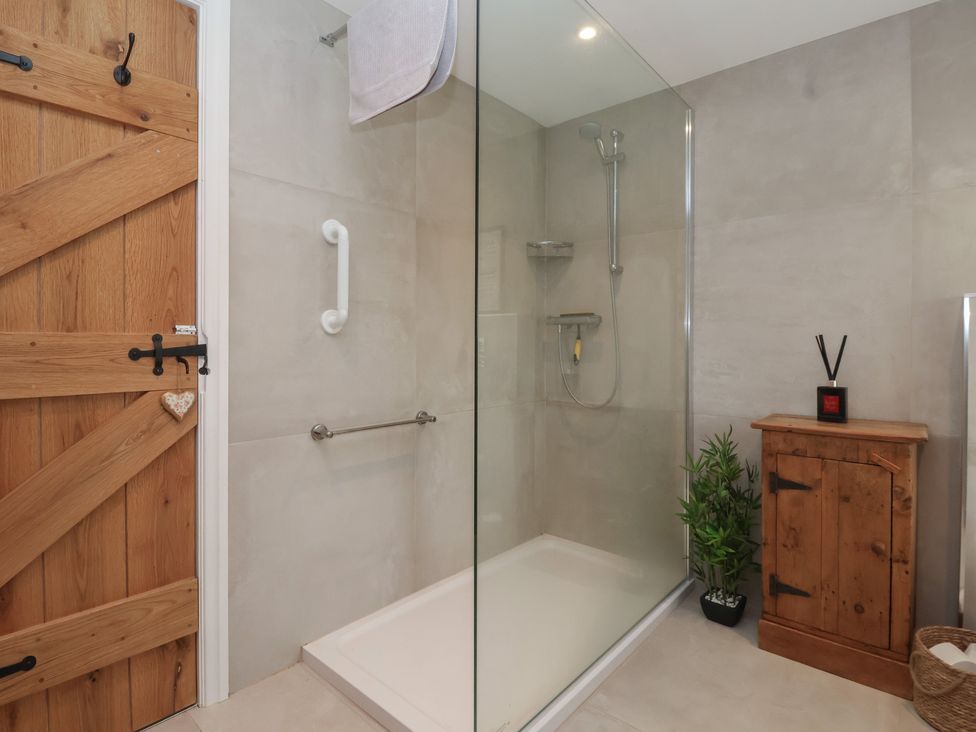 A bathroom with a shower and wooden cabinet at Maple Tree Cottage in Knaresborough
