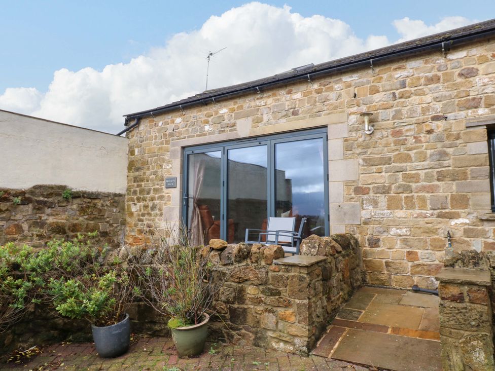 A patio area with stone wall and sliding doors at The Warren Barn in Kirkby Malzeard