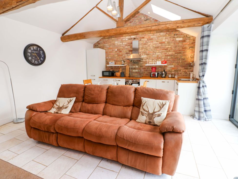 A living room with a brown sofa and kitchen area at The Holt Barn in Kirkby Malzeard