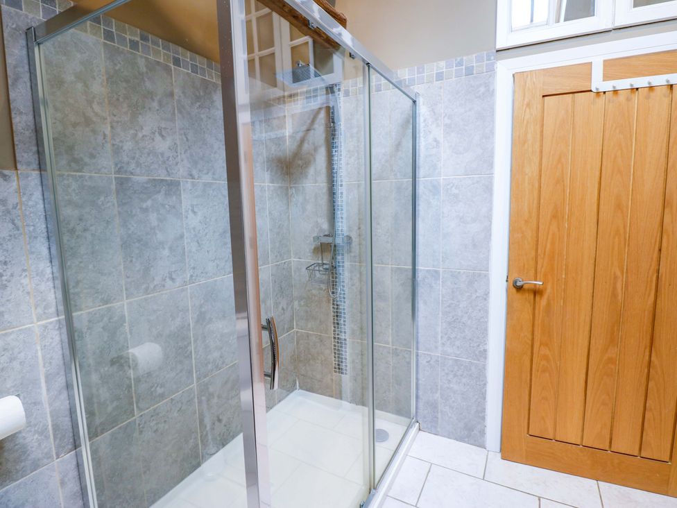 A bathroom with a walk-in shower and wooden door at The Holt Barn in Kirkby Malzeard