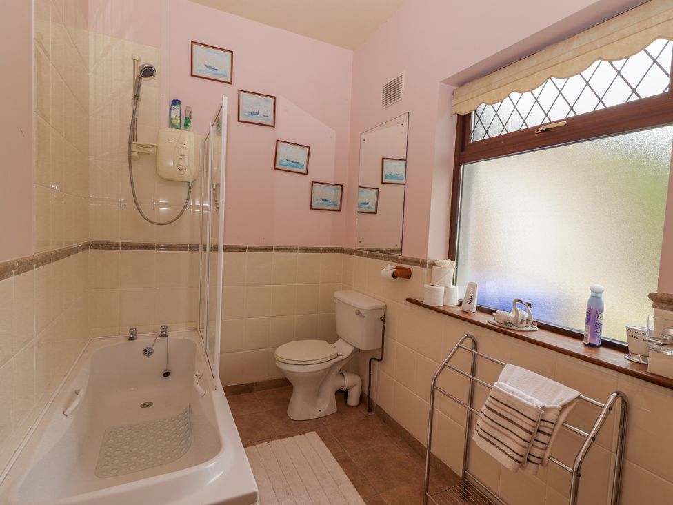 A bathroom with a bathtub, shower, toilet, and mirror at Coole Gate Lodge, Gort, County Galway