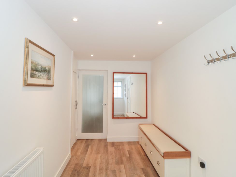 A hallway with a mirror, coat hooks, and a bench at Wellinghill Cottage at Wellinghill House in Charlton Kings