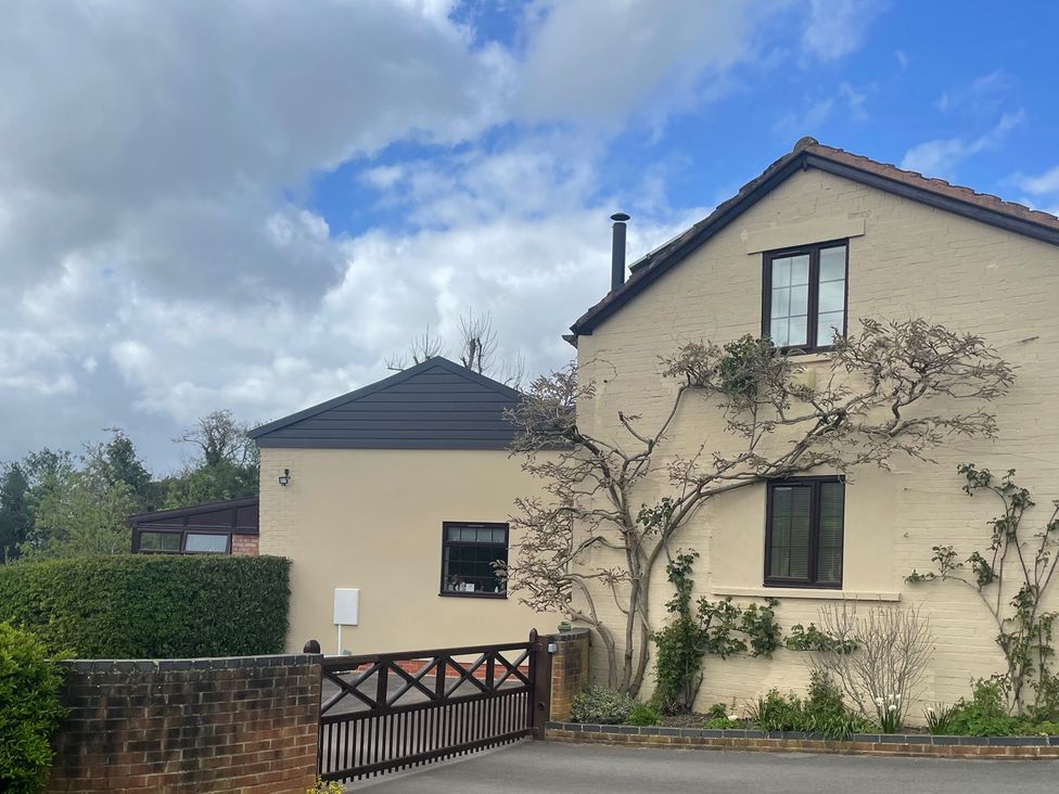 A house with a gate and surrounding plants at Wellinghill Cottage in Charlton Kings