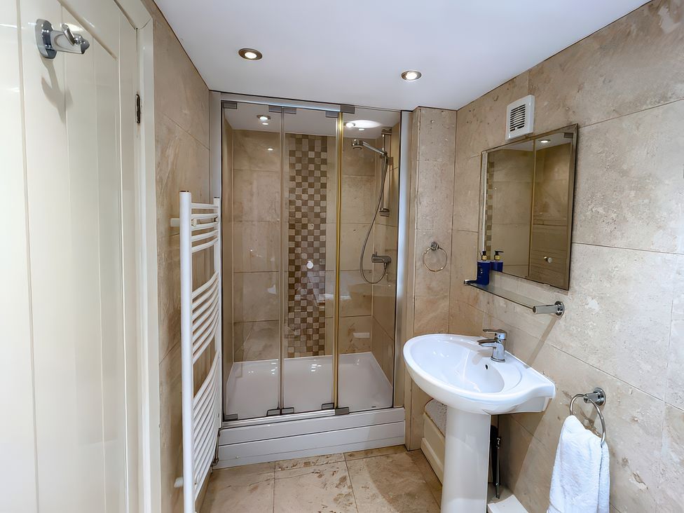 A bathroom with shower, sink, mirror, and towel warmer at Old Corner Barn, Troutbeck