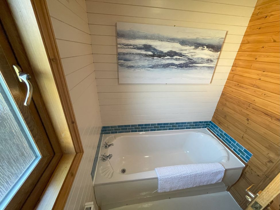 A bathroom with a bathtub, towel, and painting at Lamorna in Sennen