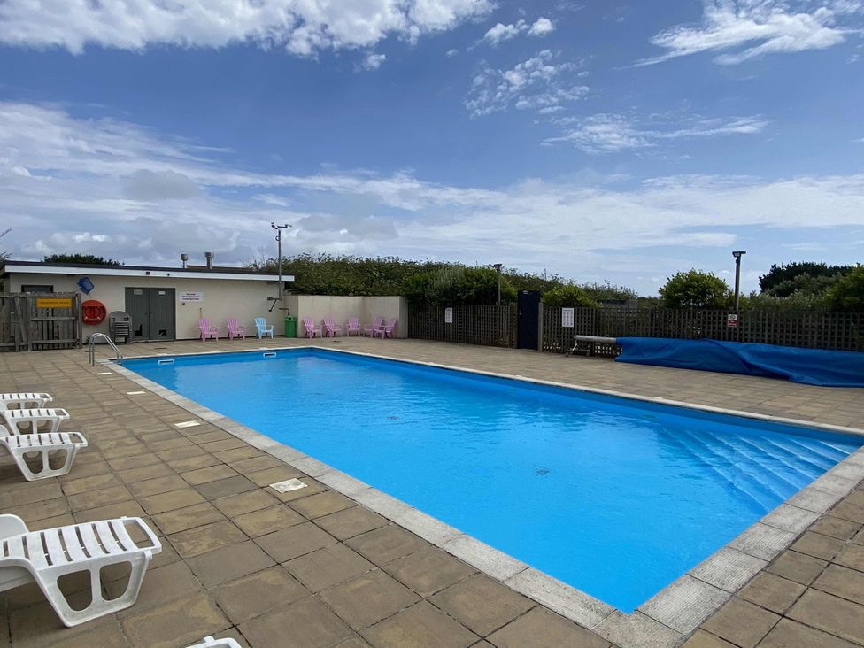 An outdoor pool area with a swimming pool and chairs at Lamorna in Sennen