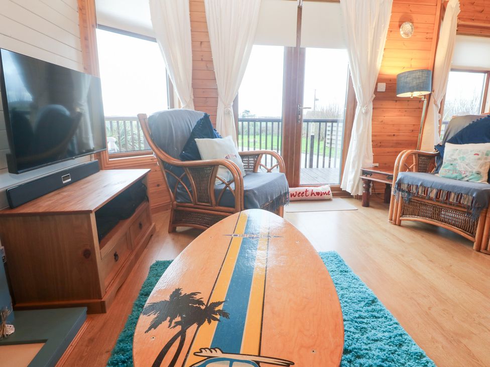 A living room with a surfboard in front of a television at Lamorna in Sennen