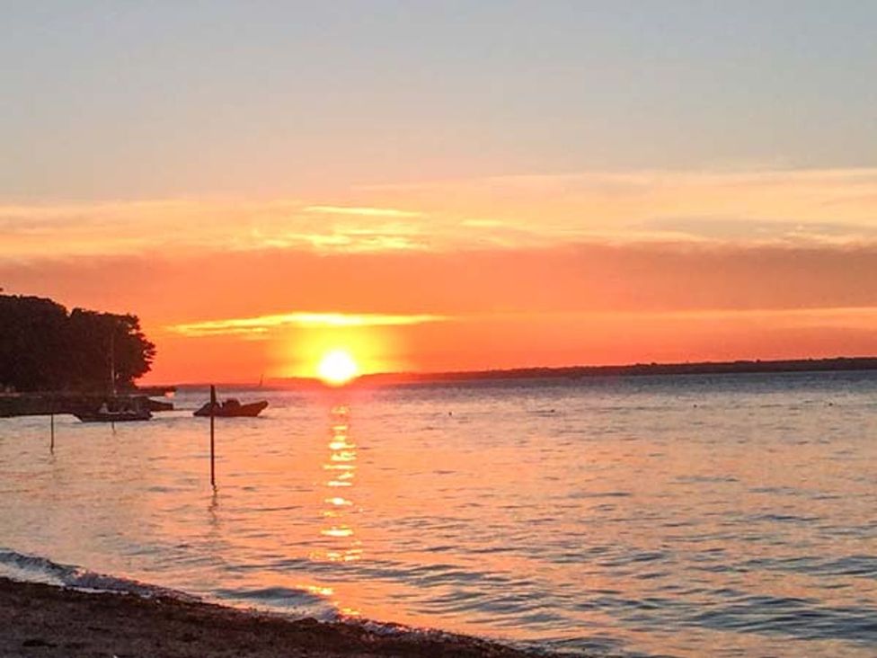 A sunset over the water with boats at Sheepwash Barn