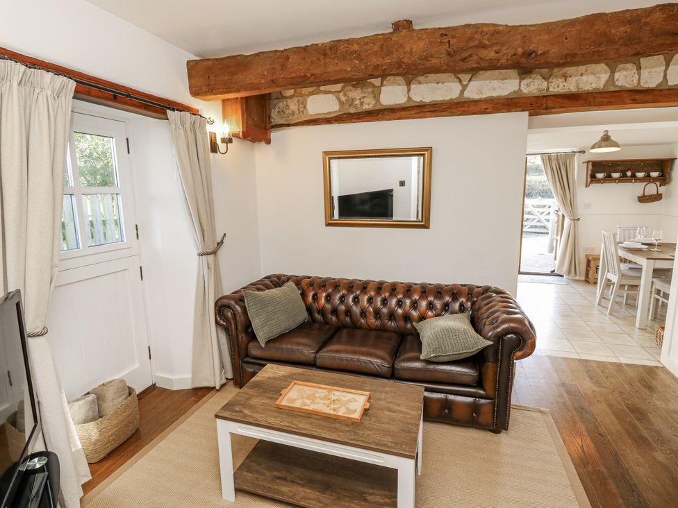 A living room with a leather sofa and dining area at Sheepwash Barn in Freshwater
