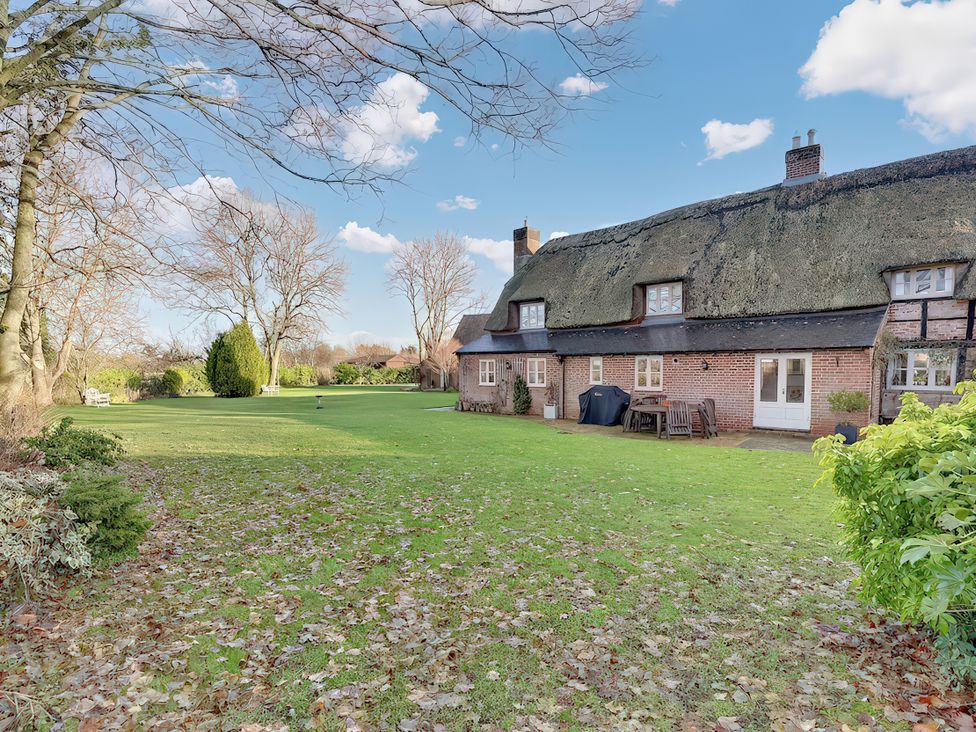 A house with a thatch roof and garden at Lake Cottage in Swindon