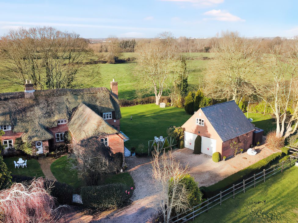 An outdoor area with a thatched roof house and a shed at Lake Cottage in Swindon