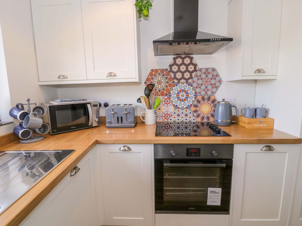 A kitchen with microwave, toaster, kettle, and patterned backsplash at 8 Watkin Street Conwy