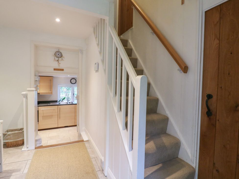 A hallway with a staircase and a view of the kitchen at Cherry Cottage