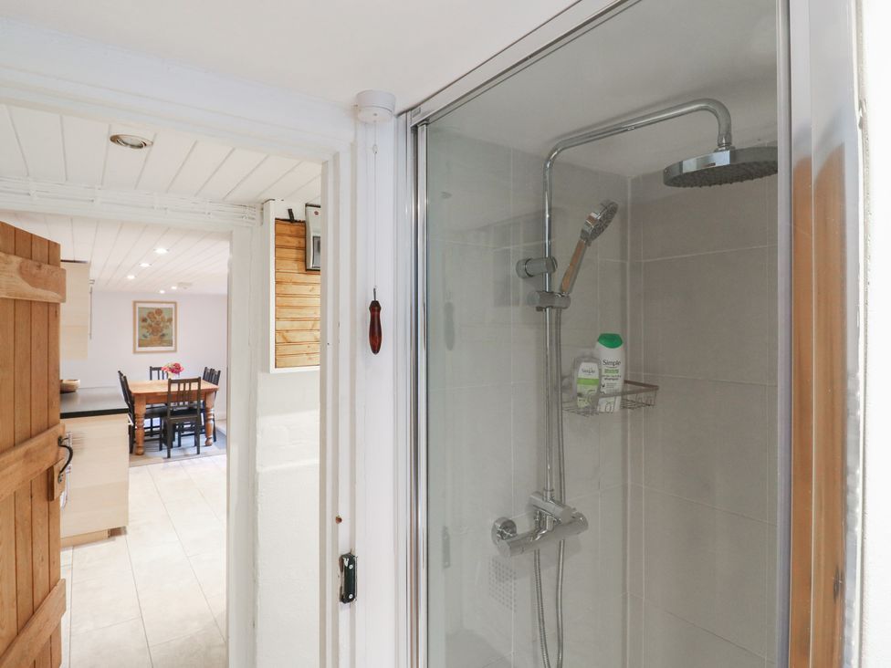 A shower with glass door and visible dining area at Cherry Cottage