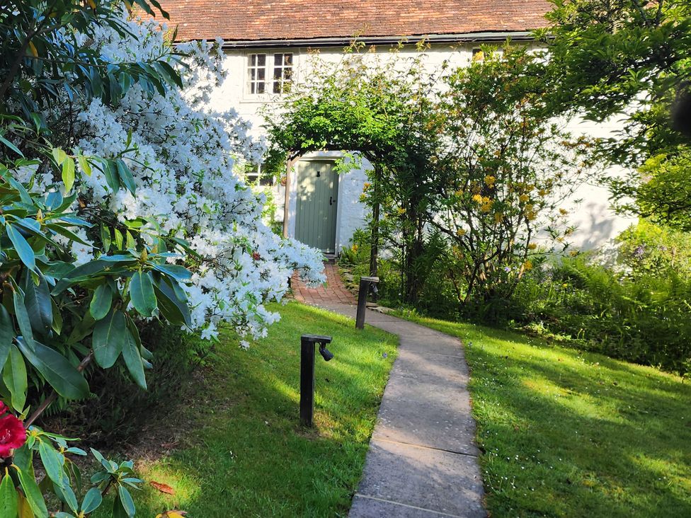 A pathway leading to a green door surrounded by shrubs at Cherry Cottage in Crowborough
