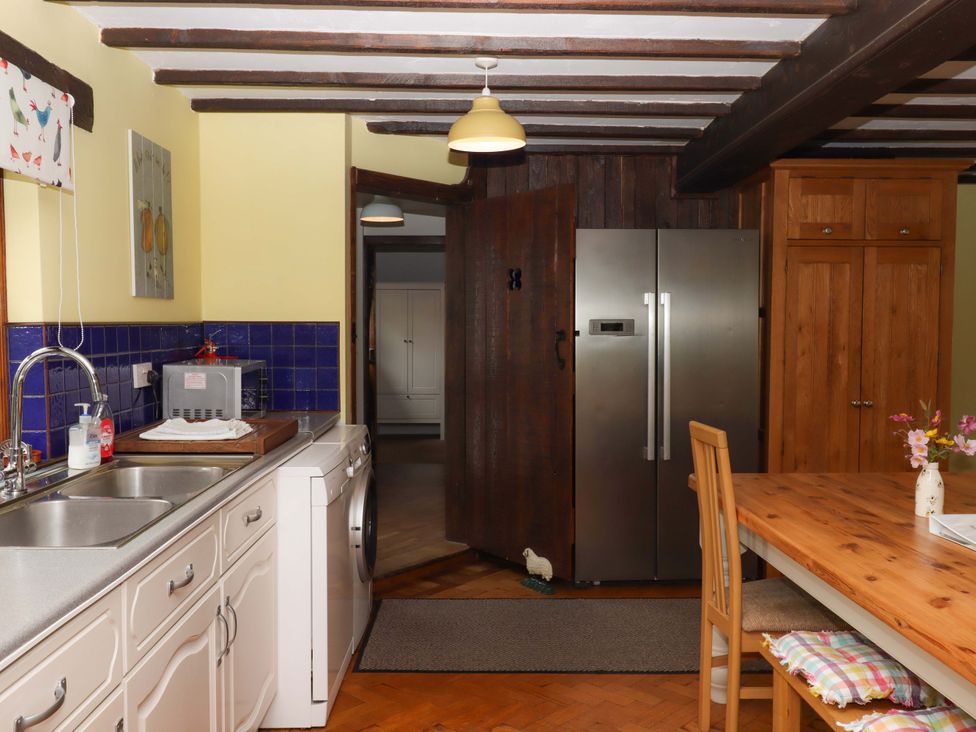 A kitchen with a sink, washing machine, and dining table at The Milking Shippon at Thorne Langtree near Great Torrington