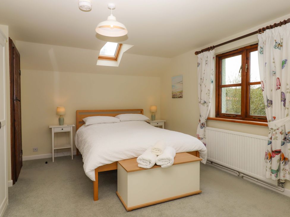 A bedroom with a bed, nightstand, and window at The Milking Shippon at Thorne near Great Torrington