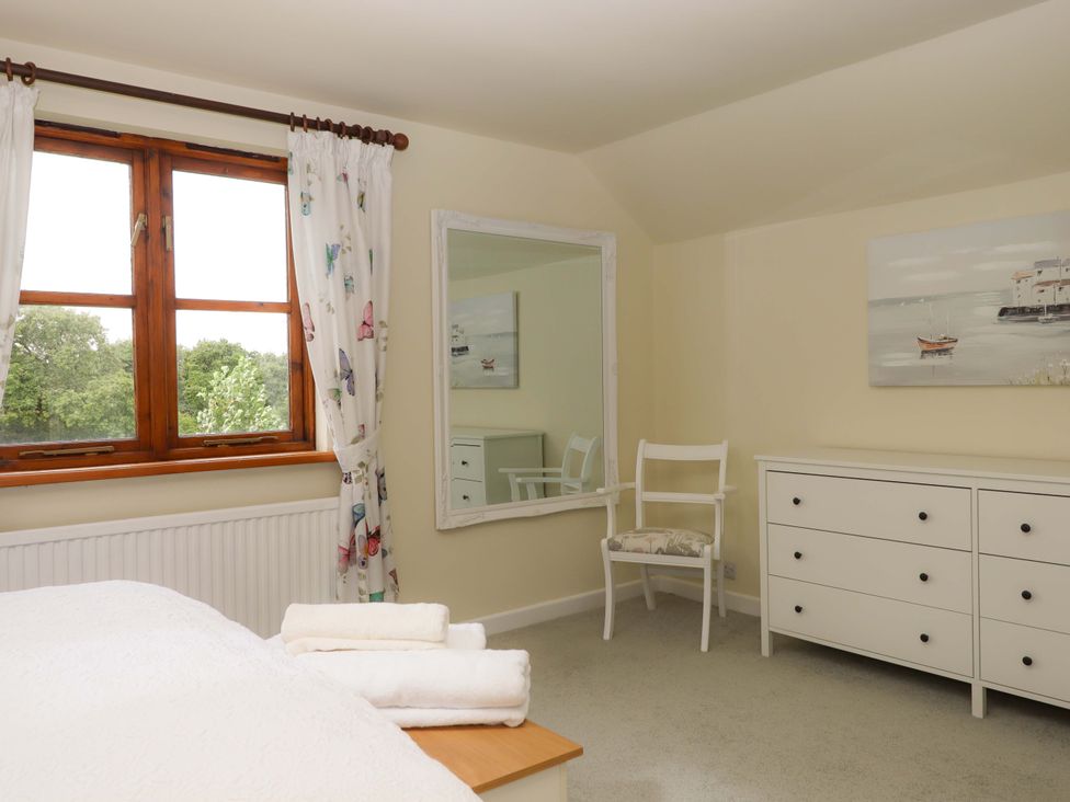 A bedroom with a window, mirror, chair, and chest of drawers at The Milking Shippon at Thorne in Langtree near Great Torrington