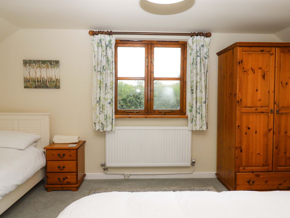 A bedroom with a bed, nightstand, wardrobe, and window at The Milking Shippon at Thorne, Langtree near Great Torrington