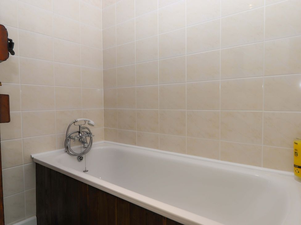 A bathroom with a bathtub and wall tiles at The Milking Shippon at Thorne, Langtree near Great Torrington