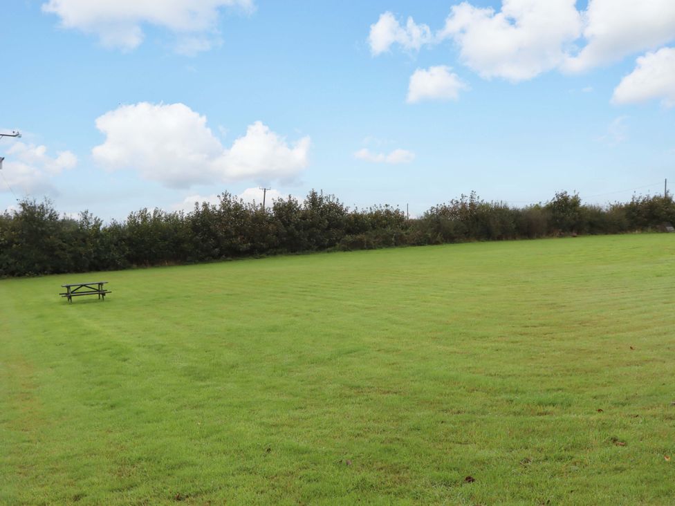 An open grassy area with a picnic table and hedge at The Milking Shippon at Thorne Langtree near Great Torrington