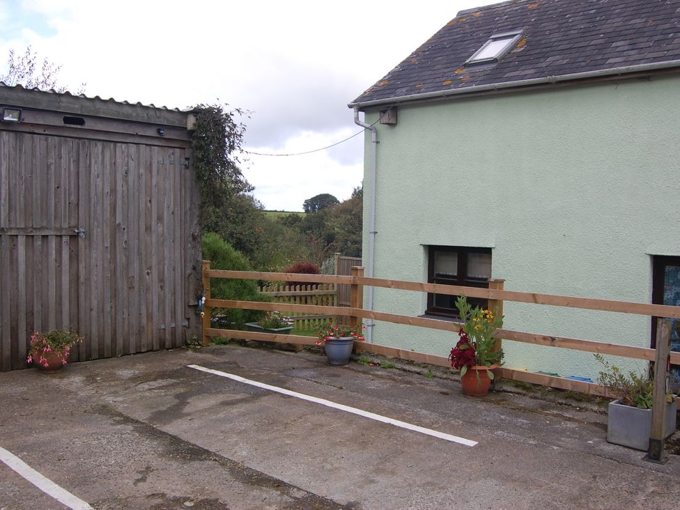 An outdoor parking area with a wooden shed and flower pots at The Milking Shippon at Thorne Langtree near Great Torrington