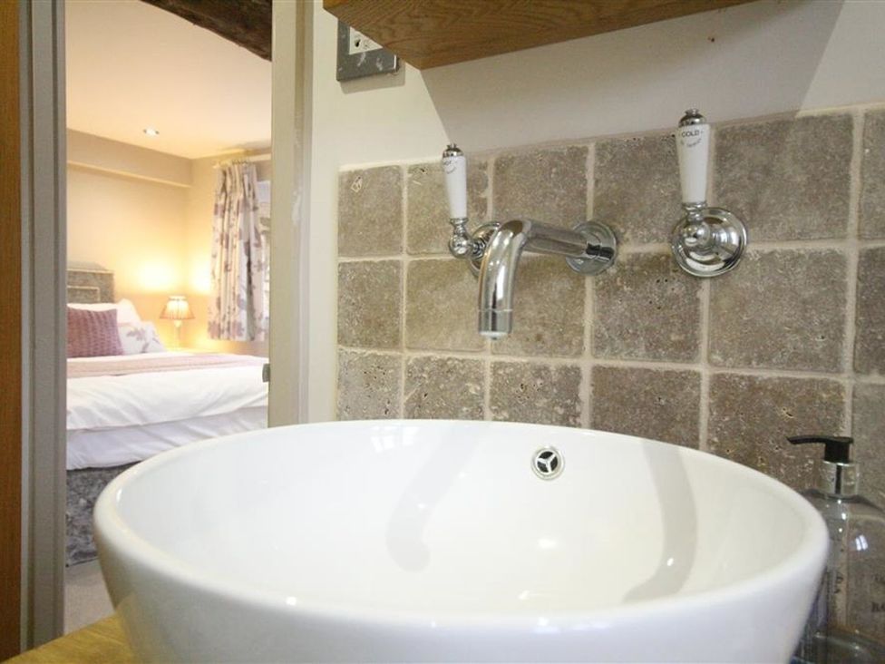 A sink and faucet with a tiled wall in a bathroom at The Coach House Burford